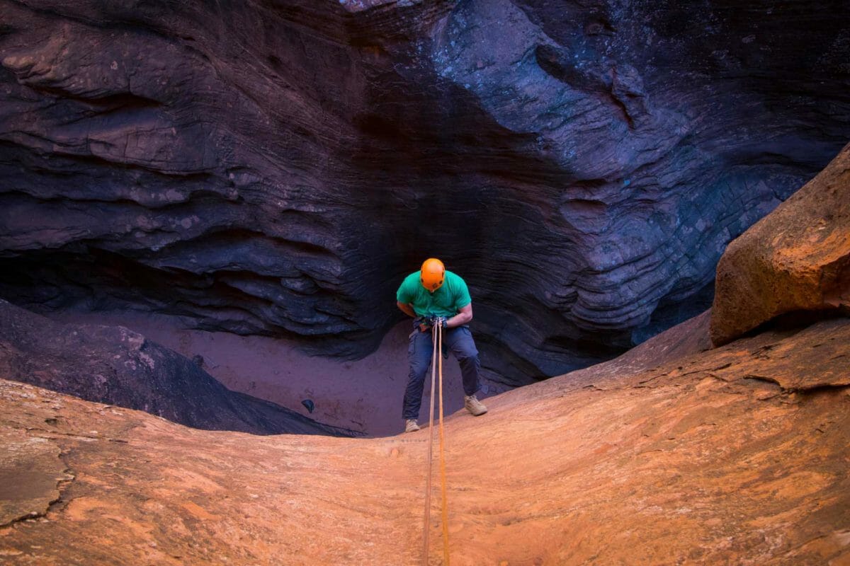 View from above of a man rappelling down into a canyon below.
