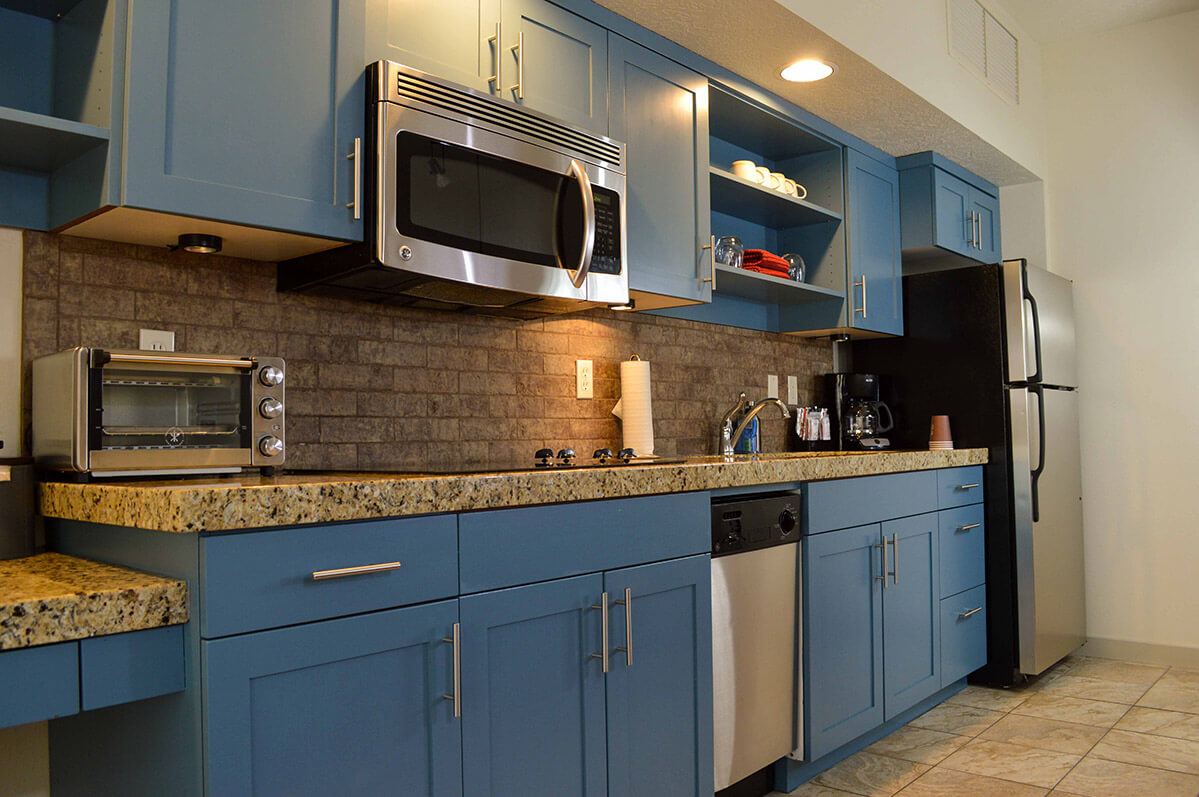 Kitchen in hotel suite with blue cabinets and granite counters and stainless steel appliances