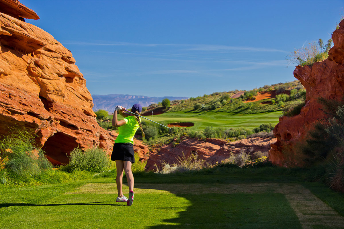 Woman golfing on desert course between red rocks