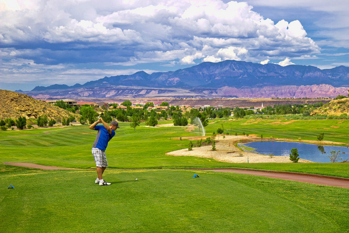 Male golfer in midswing on golf course under a blue sky with fluffy clouds.
