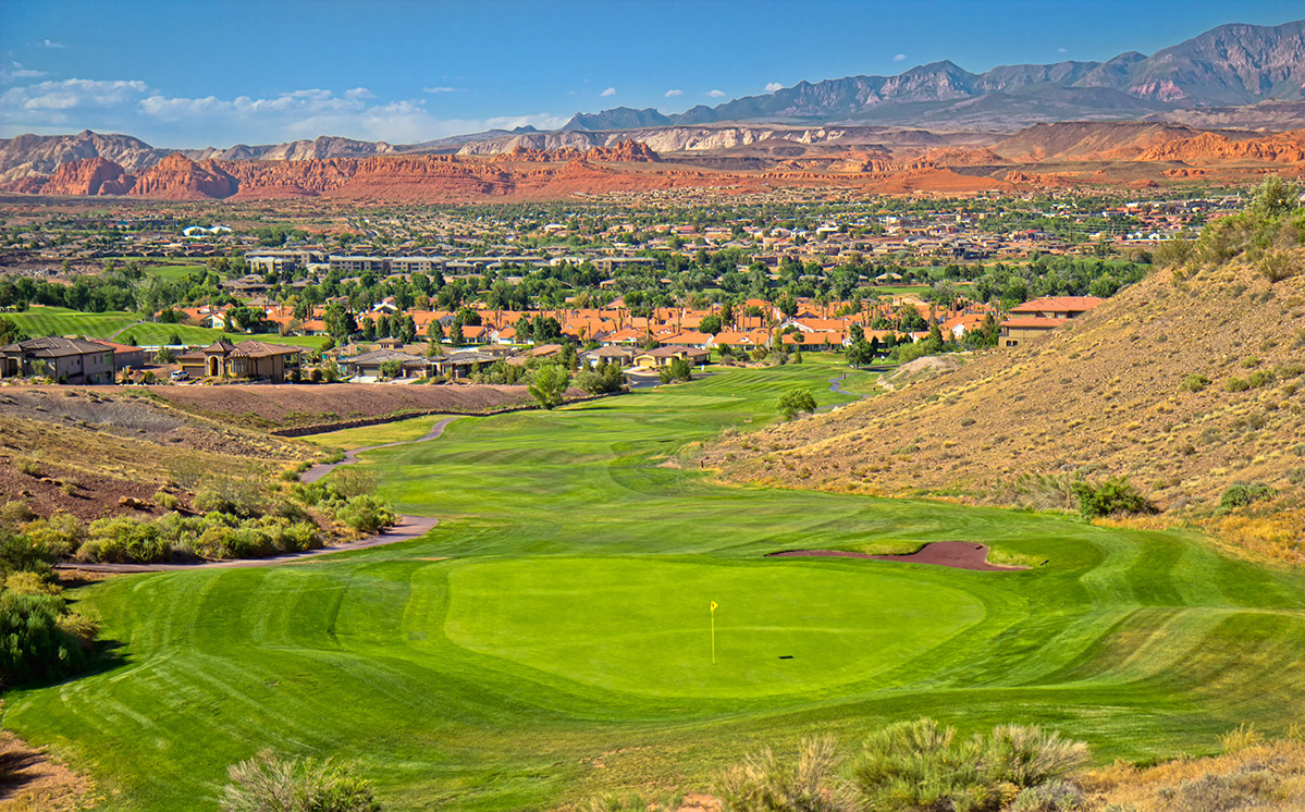 Golf course green with houses and mountains in background