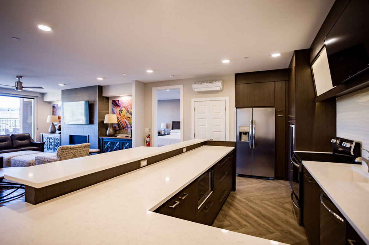Hotel room with full kitchen, stainless steel refrigerator, and view into living room and bedroom