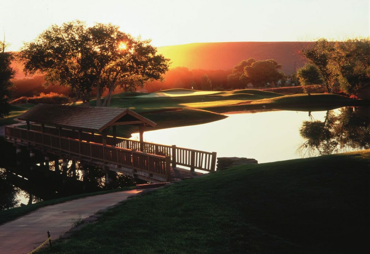 Sun rising over wooden bridge over pond at golf course.