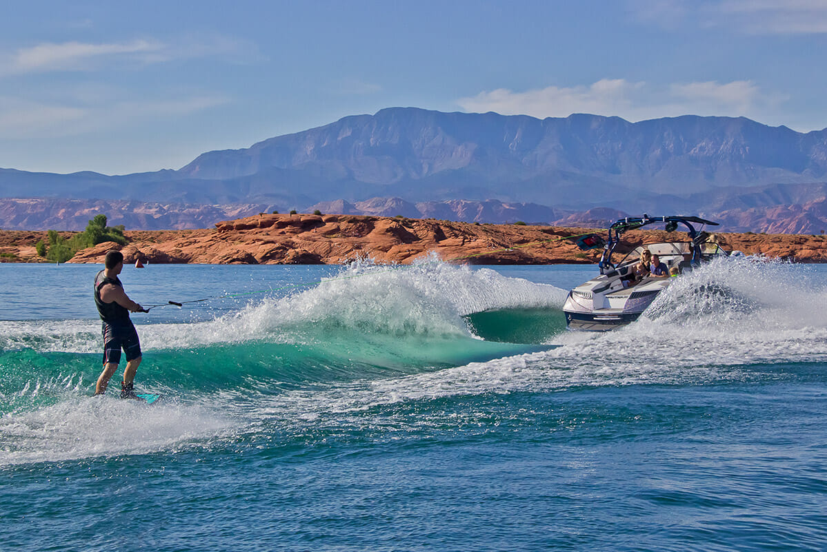 Man wakeboarding behind a boat on turquoise water.